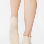 Women wearing a solid off white ivory full foot grip sock with a ruffle cuff and with a red cherry on the top of the toes, made for pilates, barre, yoga, and beyond.
