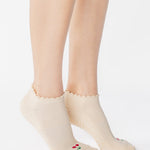 Women wearing a solid off white ivory full foot grip sock with a ruffle cuff and with a red cherry on the top of the toes, made for pilates, barre, yoga, and beyond.