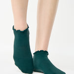 Women wearing a solid forest green full foot grip sock with a playful ruffle cuff made for Pilates, Barre, Yoga, and Beyond. 