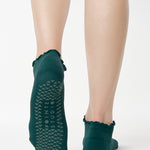 Women wearing a solid forest green full foot grip sock with a playful ruffle cuff made for Pilates, Barre, Yoga, and Beyond. 