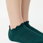 Women wearing a solid forest green full foot grip sock with a playful ruffle cuff made for Pilates, Barre, Yoga, and Beyond. 