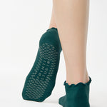 Women wearing a solid forest green full foot grip sock with a playful ruffle cuff made for Pilates, Barre, Yoga, and Beyond. 