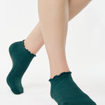 Women wearing a solid forest green full foot grip sock with a playful ruffle cuff made for Pilates, Barre, Yoga, and Beyond. 