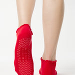 Women wearing a solid bright red full foot grip sock with a playful ruffle cuff made for Pilates, Barre, Yoga, and Beyond. 