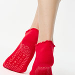 Women wearing a solid bright red full foot grip sock with a playful ruffle cuff made for Pilates, Barre, Yoga, and Beyond. 