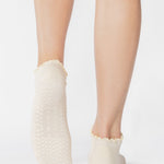 Women wearing a solid white full foot grip sock with a playful ruffle cuff made for Pilates, Barre, Yoga, and Beyond. 