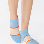 Woman wearing a light blue full foot grip sock with a bold off white stripe with a contrasting orange outline, made for pilates, barre, yoga, and beyond. 