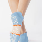 Woman wearing a light blue full foot grip sock with a bold off white stripe with a contrasting orange outline, made for pilates, barre, yoga, and beyond. 