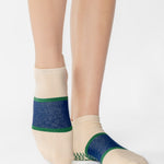 Woman wearing an off white full foot grip sock with a bold navy blue stripe with a contrasting green outline, made for pilates, barre, yoga, and beyond. 
