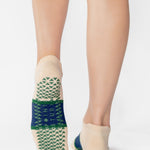 Woman wearing an off white full foot grip sock with a bold navy blue stripe with a contrasting green outline, made for pilates, barre, yoga, and beyond. 