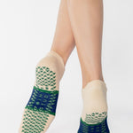 Woman wearing an off white full foot grip sock with a bold navy blue stripe with a contrasting green outline, made for pilates, barre, yoga, and beyond. 