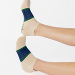 Woman wearing an off white full foot grip sock with a bold navy blue stripe with a contrasting green outline, made for pilates, barre, yoga, and beyond. 