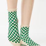Woman wearing a green with beige ankle grip sock with a ruffled cuff made for Pilates, Barre, Yoga, and beyond. 