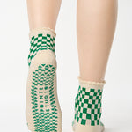 Woman wearing a green with beige ankle grip sock with a ruffled cuff made for Pilates, Barre, Yoga, and beyond. 