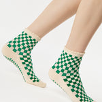 Woman wearing a green with beige ankle grip sock with a ruffled cuff made for Pilates, Barre, Yoga, and beyond. 