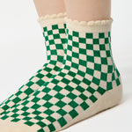 Woman wearing a green with beige ankle grip sock with a ruffled cuff made for Pilates, Barre, Yoga, and beyond. 