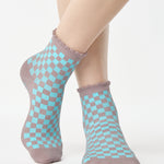 Woman wearing a checkered light blue with gray ankle grip sock with a ruffled cuff made for Pilates, Barre, Yoga, and beyond. 