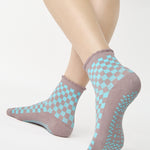 Woman wearing a checkered light blue with gray ankle grip sock with a ruffled cuff made for Pilates, Barre, Yoga, and beyond. 