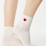 Women wearing a solid white ankle grip sock with a red heart on the ankle made for Pilates, Barre, Yoga, and beyond. 