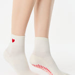 Women wearing a solid white ankle grip sock with a red heart on the ankle made for Pilates, Barre, Yoga, and beyond. 