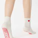 Women wearing a solid white ankle grip sock with a red heart on the ankle made for Pilates, Barre, Yoga, and beyond. 