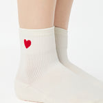 Women wearing a solid white ankle grip sock with a red heart on the ankle made for Pilates, Barre, Yoga, and beyond. 
