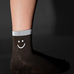 Women wearing brown ankle grip socks with white happy face and reflective stripe for running. 