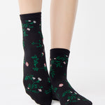Woman wearing a black ankle grip sock with green rose vines and pink flowers made for Pilates, Barre, Yoga, and beyond.