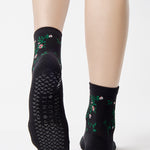 Woman wearing a black ankle grip sock with green rose vines and pink flowers made for Pilates, Barre, Yoga, and beyond.
