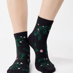 Woman wearing a black ankle grip sock with green rose vines and pink flowers made for Pilates, Barre, Yoga, and beyond.