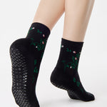 Woman wearing a black ankle grip sock with green rose vines and pink flowers made for Pilates, Barre, Yoga, and beyond.