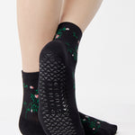 Woman wearing a black ankle grip sock with green rose vines and pink flowers made for Pilates, Barre, Yoga, and beyond.