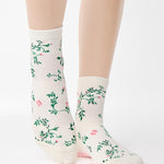 Woman wearing a white ankle grip sock with green rose vines and pink flowers made for Pilates, Barre, Yoga, and beyond.