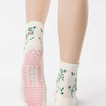 Woman wearing a white ankle grip sock with green rose vines and pink flowers made for Pilates, Barre, Yoga, and beyond.