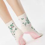 Woman wearing a white ankle grip sock with green rose vines and pink flowers made for Pilates, Barre, Yoga, and beyond.