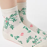 Woman wearing a white ankle grip sock with green rose vines and pink flowers made for Pilates, Barre, Yoga, and beyond.