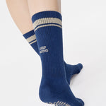 Woman wearing a navy blue crew grip sock with "keep going" embroidered in the back part of the ankle/calf area, made for Pilates, Barre, Yoga, and beyond. 
