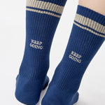 Woman wearing a navy blue crew grip sock with "keep going" embroidered in the back part of the ankle/calf area, made for Pilates, Barre, Yoga, and beyond. 