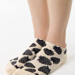 Women wearing a white full foot grip sock with black strawberries all around. 