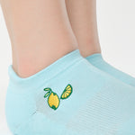 Women wearing a light blue full foot grip sock with a yellow lemon motif near the cuff made for Pilates, Barre, Yoga, and beyond. 