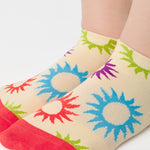 Women wearing an off white full foot grip sock with colorful suns all around made for pilates, yoga, barre, and beyond.