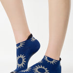 Women wearing a navy full foot grip sock with white suns all around made for pilates, yoga, barre, and beyond.