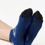 Women wearing a navy full foot grip sock with white suns all around made for pilates, yoga, barre, and beyond.