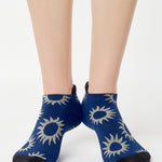 Women wearing a navy full foot grip sock with white suns all around made for pilates, yoga, barre, and beyond.