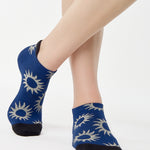 Women wearing a navy full foot grip sock with white suns all around made for pilates, yoga, barre, and beyond.