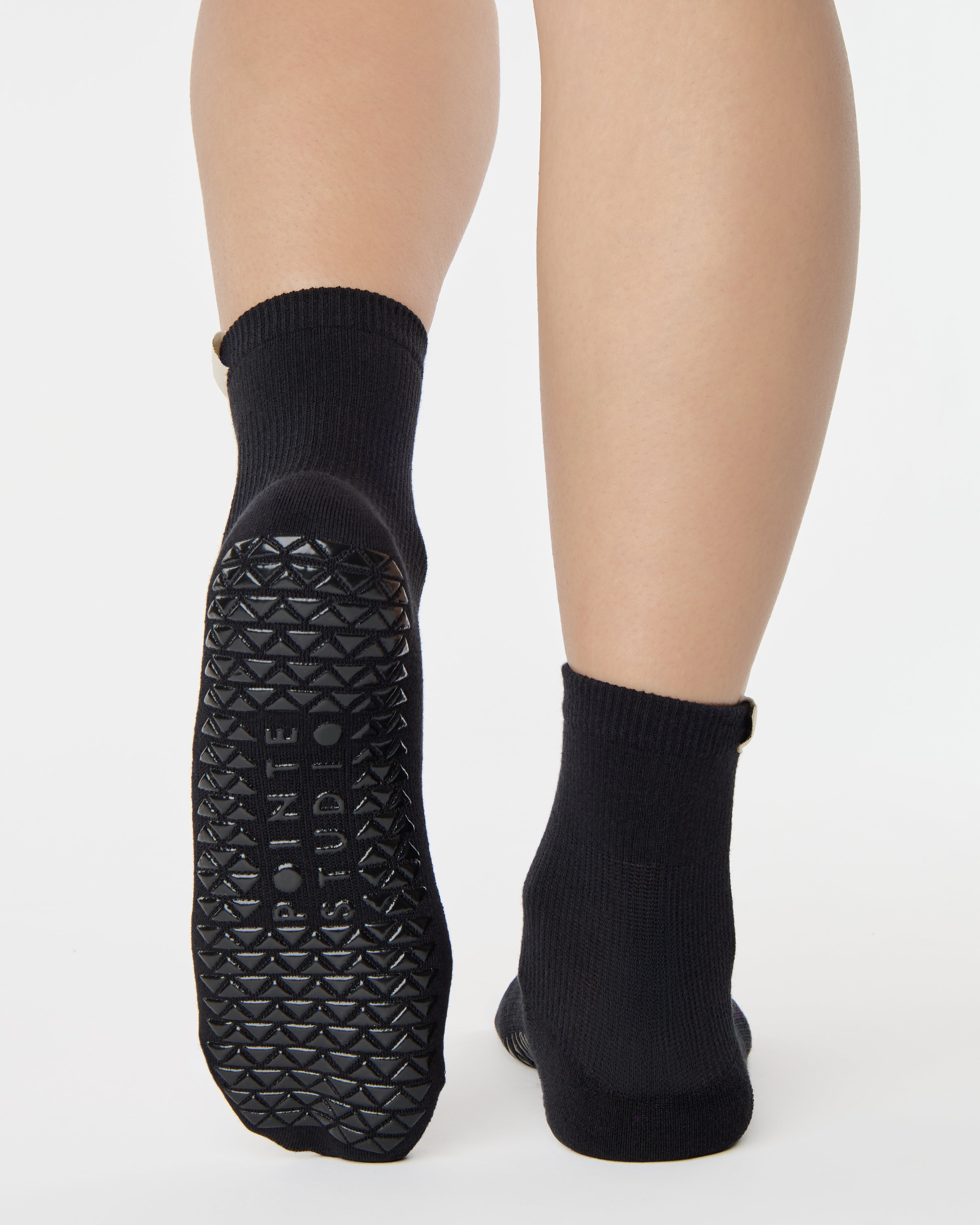 Woman wearing a solid black ankle grip sock with gemini zodiac sign embroidered on the side. Made for pilates, barre, yoga, and beyond. 