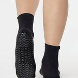 Woman wearing a solid black ankle grip sock with pisces zodiac sign embroidered on the side. Made for pilates, barre, yoga, and beyond. 