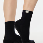 Woman wearing a solid black ankle grip sock with aquarius zodiac sign embroidered on the side. Made for pilates, barre, yoga, and beyond. 