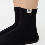 Woman wearing a solid black ankle grip sock with aquarius zodiac sign embroidered on the side. Made for pilates, barre, yoga, and beyond. 