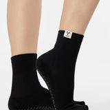Woman wearing a solid black ankle grip sock with aries zodiac sign embroidered on the side. Made for pilates, barre, yoga, and beyond. 